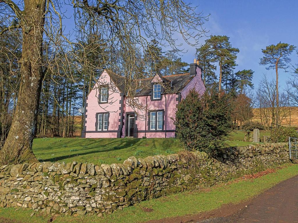 una casa rosa con un muro di pietra e un albero di The Glen Farmhouse a Crocketford