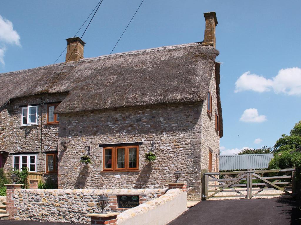 an old stone house with a thatched roof at Two Bridge Cottage in Winsham