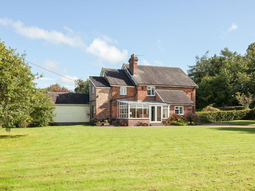 een bakstenen huis met een groot gazon ervoor bij Fir Tree Cottage in Standon