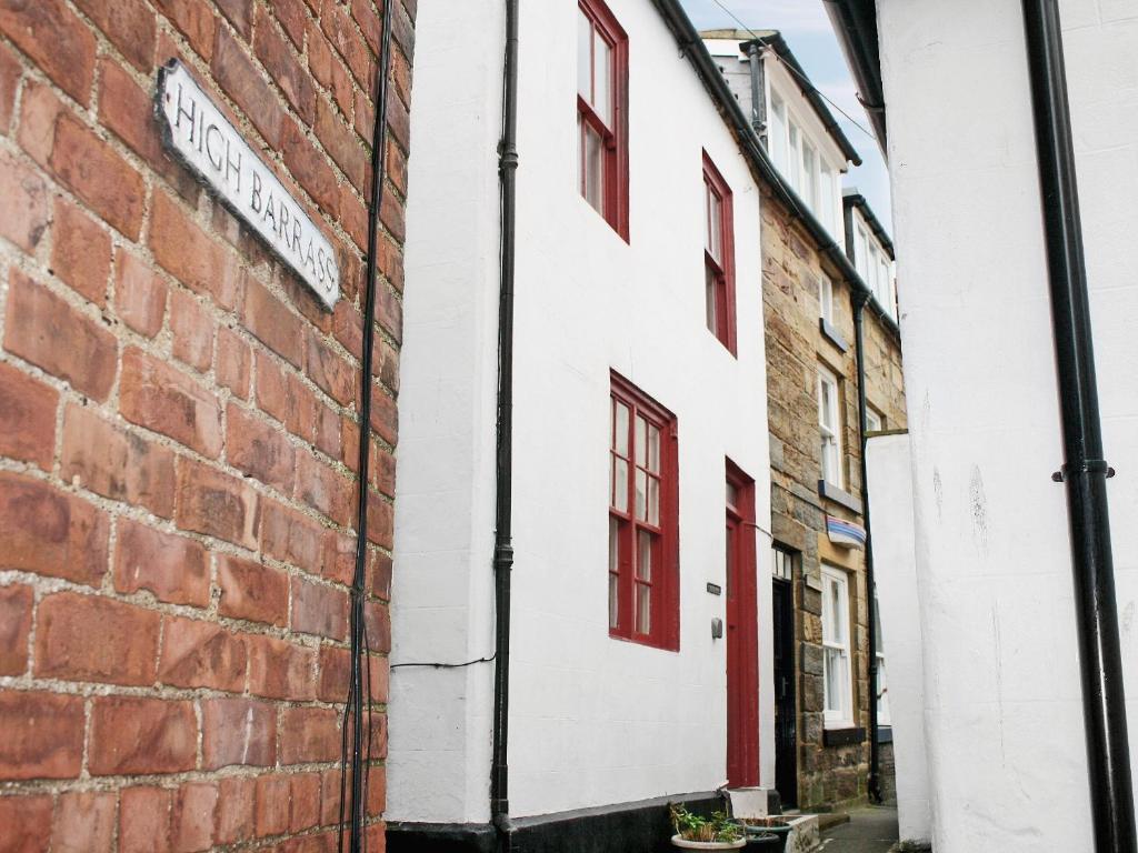 a white building with red windows and a brick wall at Castleton House in Staithes
