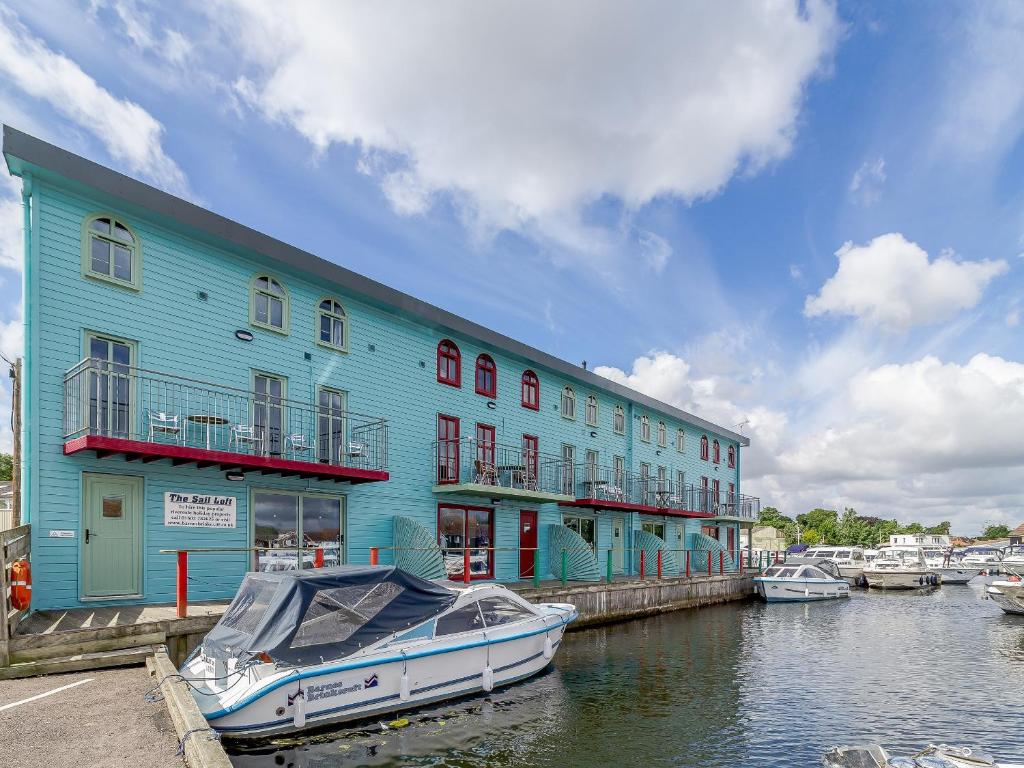 a boat is docked next to a blue building at Jib Sail-18148 in Wroxham