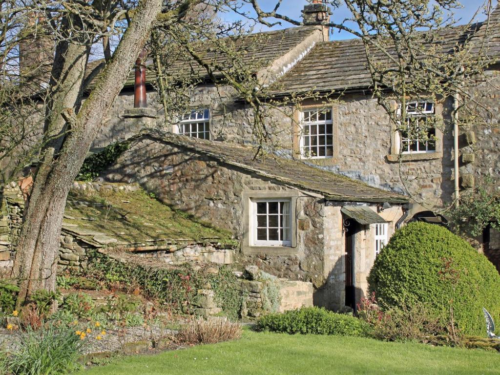 an old stone house with a tree in front of it at Inglenook Cottage in Kettlewell