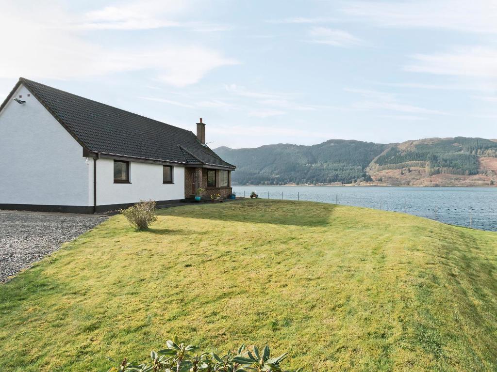 a house on a grassy hill next to a body of water at Loch Duich Cottage in Inverinate