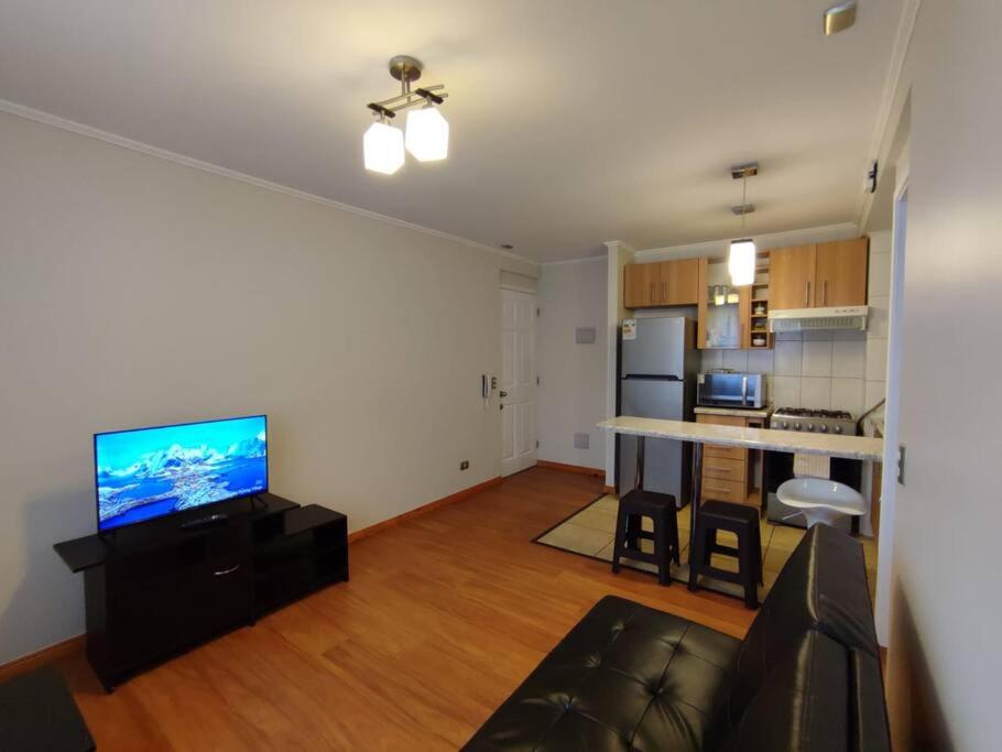 een woonkamer met een bank en een televisie en een keuken bij Departamento amoblado muy cómodo in Puerto Montt