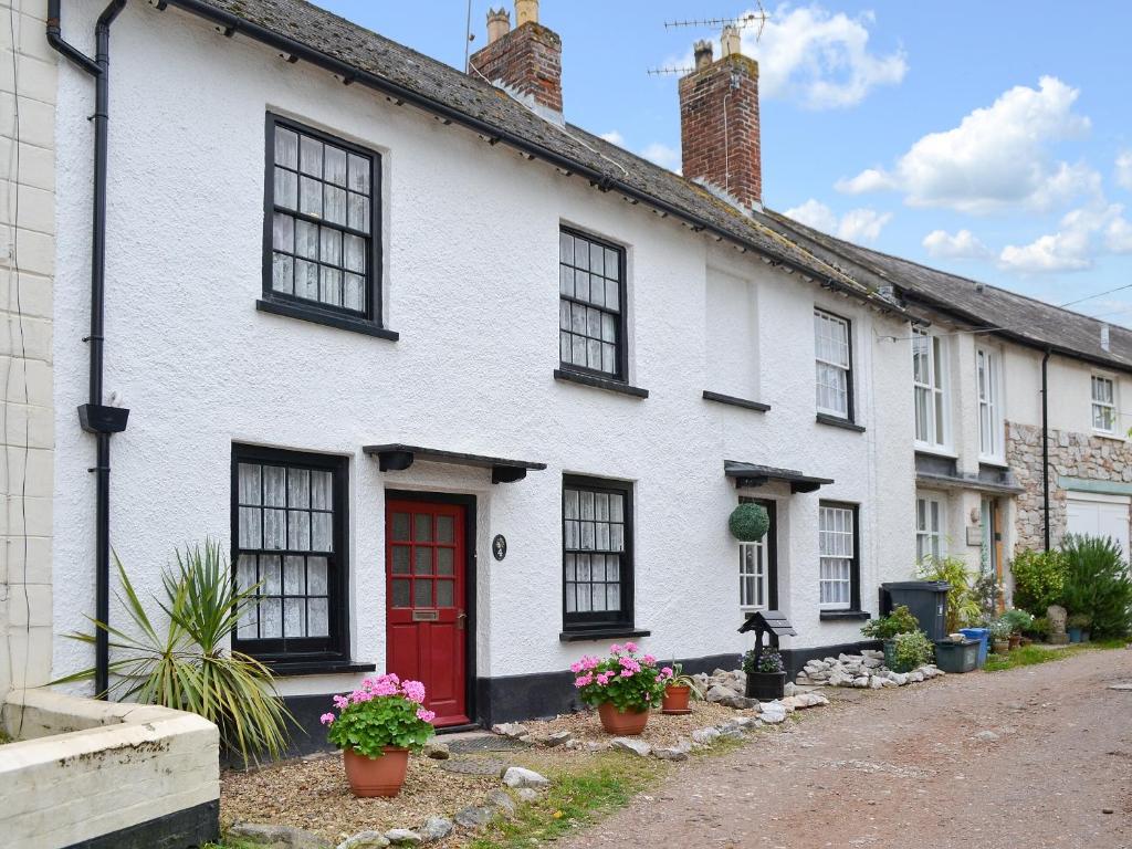 een wit huis met zwarte ramen en een rode deur bij Pebbles in Lympstone