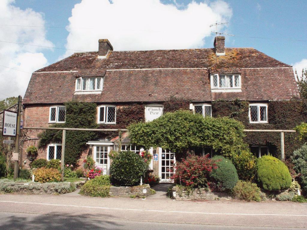 une grande maison en briques avec des buissons devant elle dans l'établissement Churchview House, à Winterborne Abbas