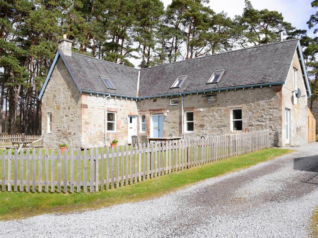 una antigua casa de piedra con una valla de madera en Birch Cottage, en Glenrossal