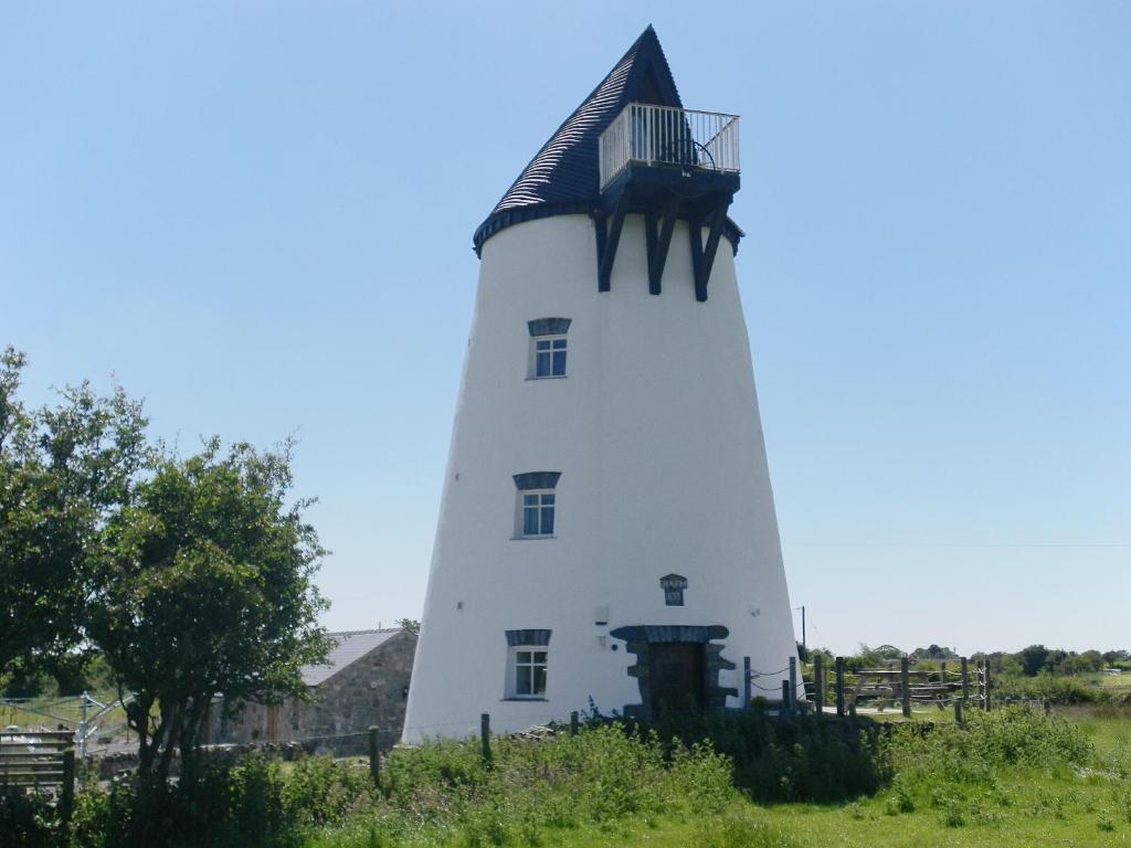 um farol branco com um telhado preto em The Windmill em Coedana