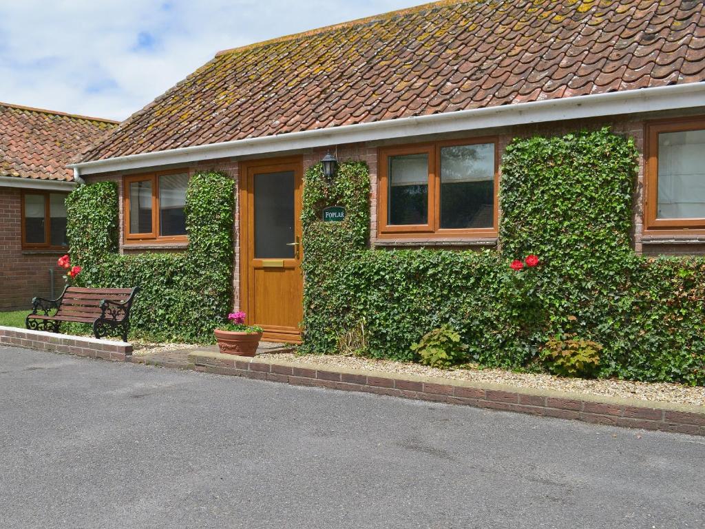 une maison recouverte de lierre avec un banc devant elle dans l'établissement Poplar Cottage, à Cote