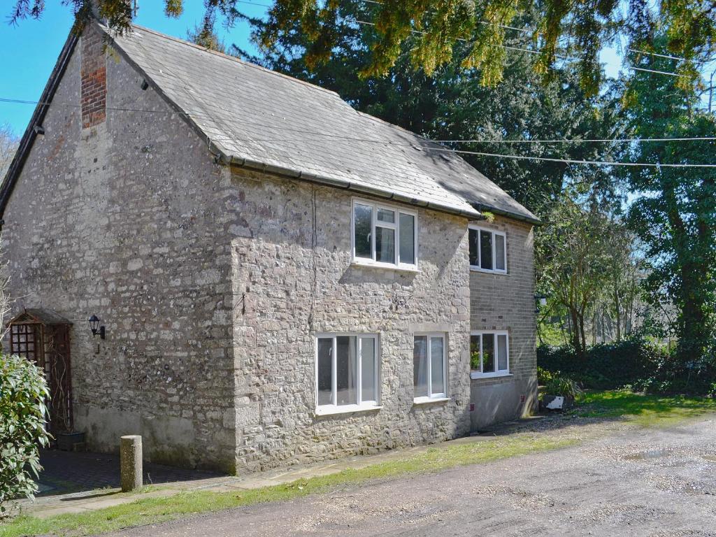 an old stone building with white windows on a street at Mill Cottage in Winterborne Steepleton