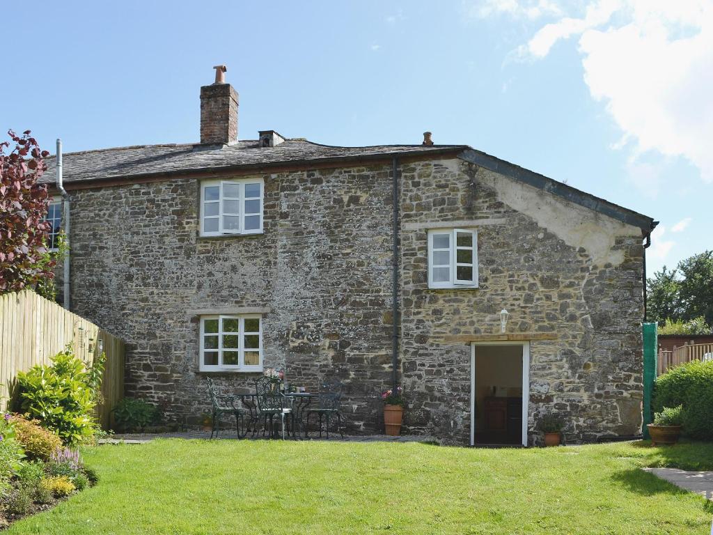 an old stone house with tables and chairs in a yard at Barton Cottage in North Petherwin