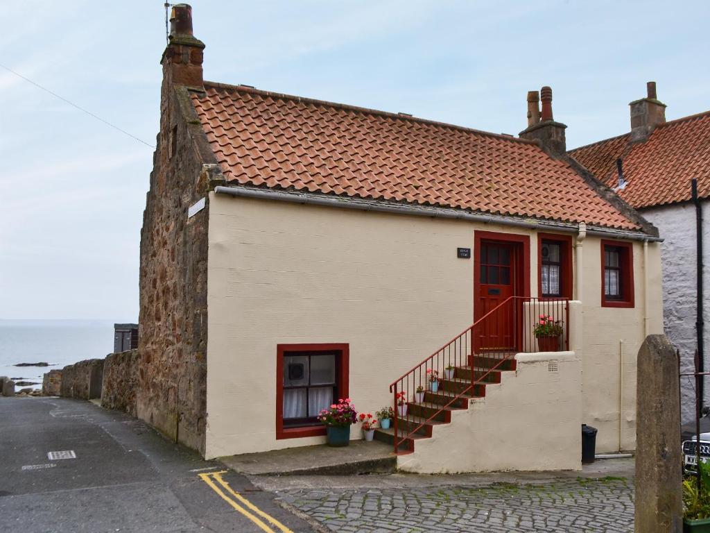 een klein huis met een rode deur en een trap bij High Tide in Cellardyke