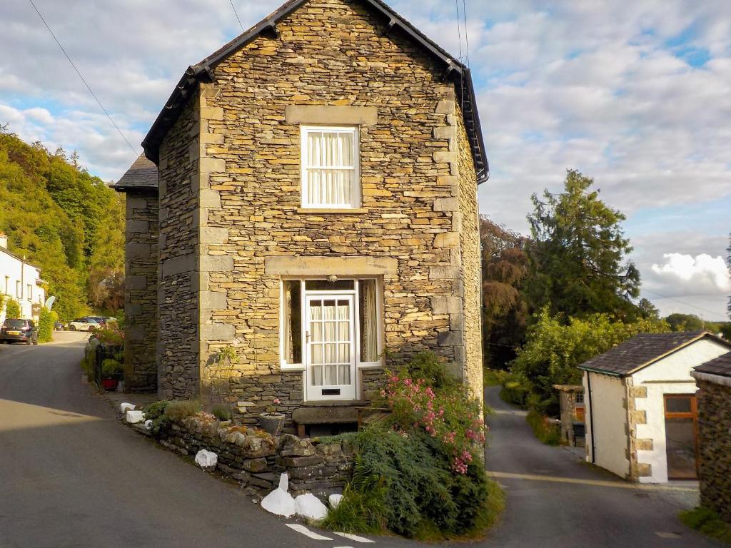 a stone house with a white door on a street at Letterbox Cottage in Far Sawrey