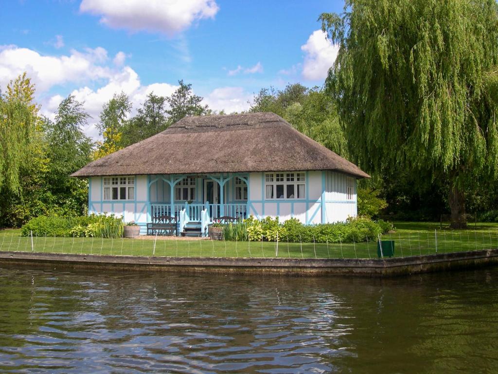 a house with a thatched roof next to a river at Leisure Hour in Wroxham