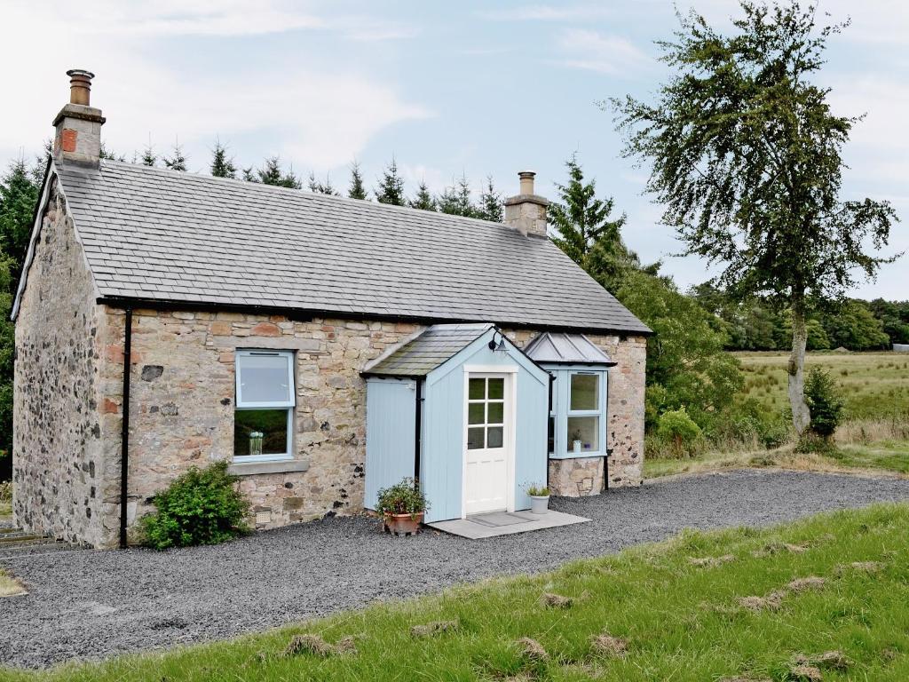 a stone cottage with a white door on a gravel driveway at Heathfield in Denholm