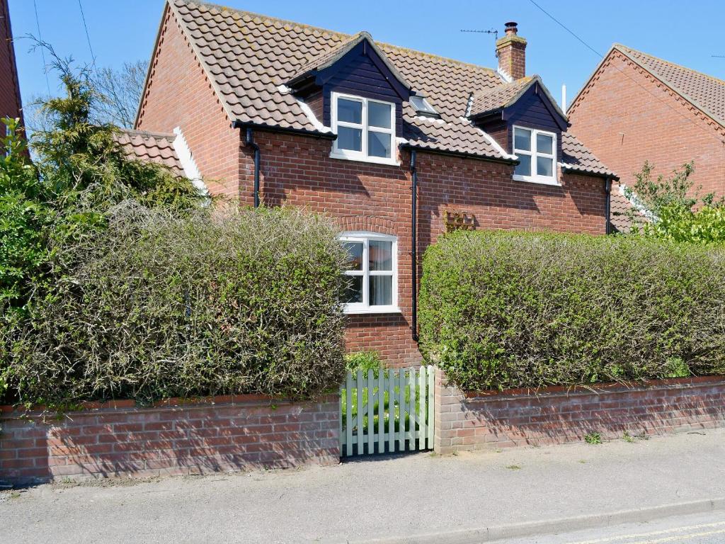 a brown brick house with a fence and bushes at Dormouse Cottage in Sea Palling