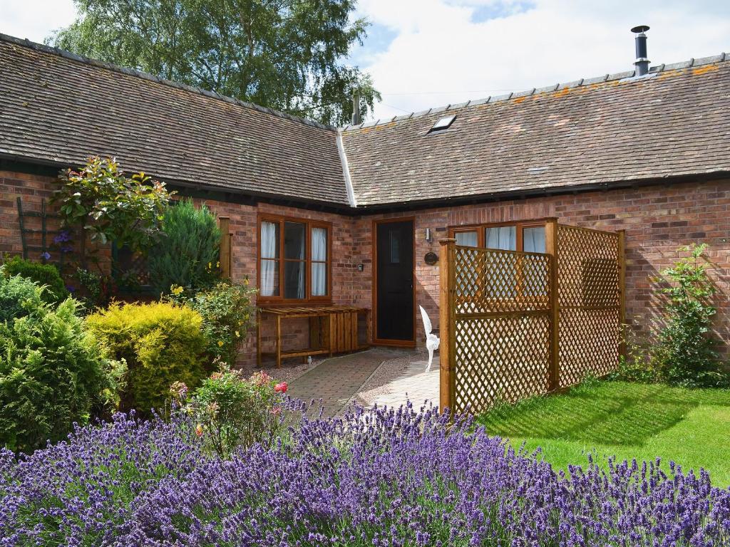 a brick house with a garden and purple flowers at Apple Cottage in Culmington