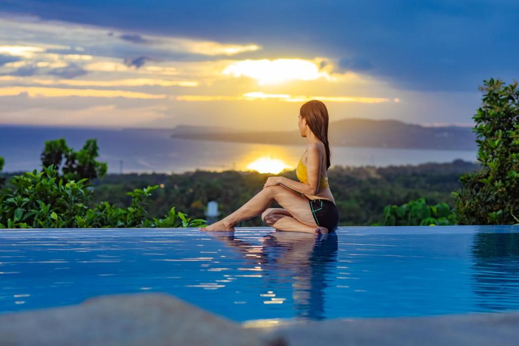 a woman sitting on the edge of a swimming pool with the sunset at Marqis Sunrise Sunset Resort and Spa in Baclayon