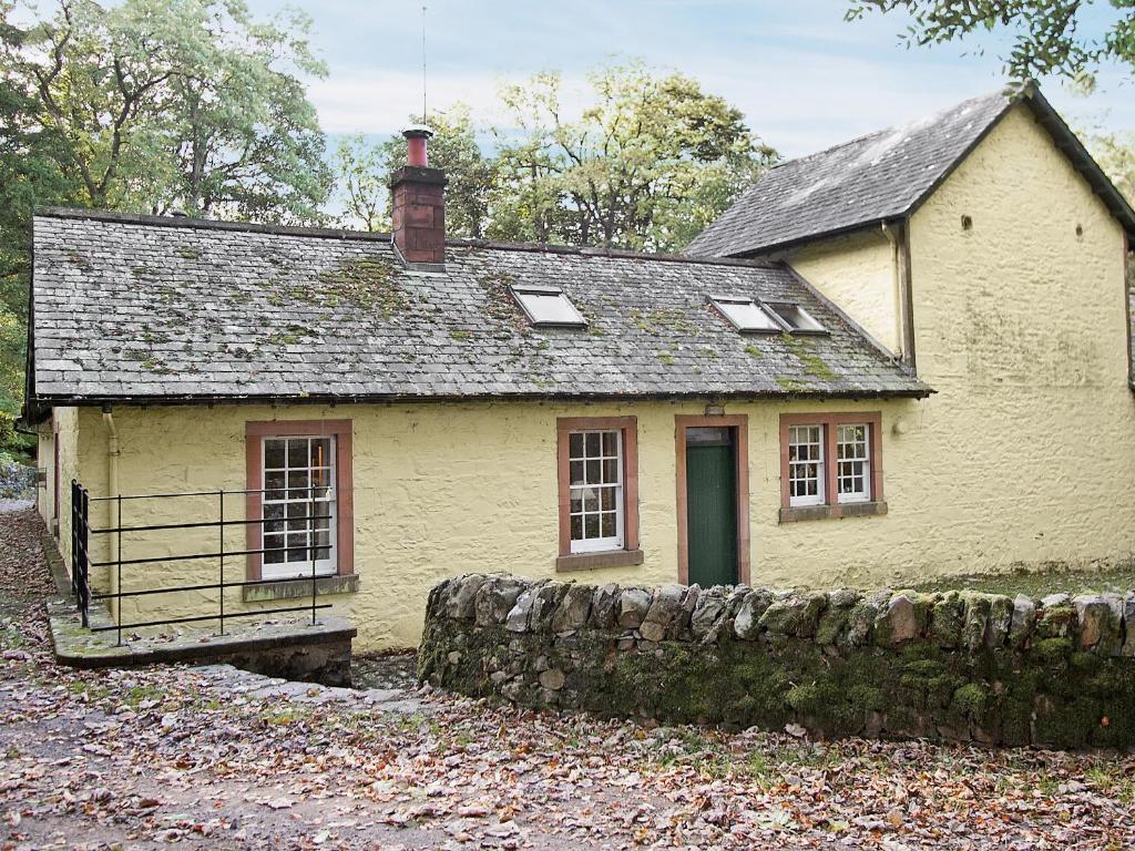 una vecchia casa gialla con un muro di pietra di Stables Cottage-uud a Corsock