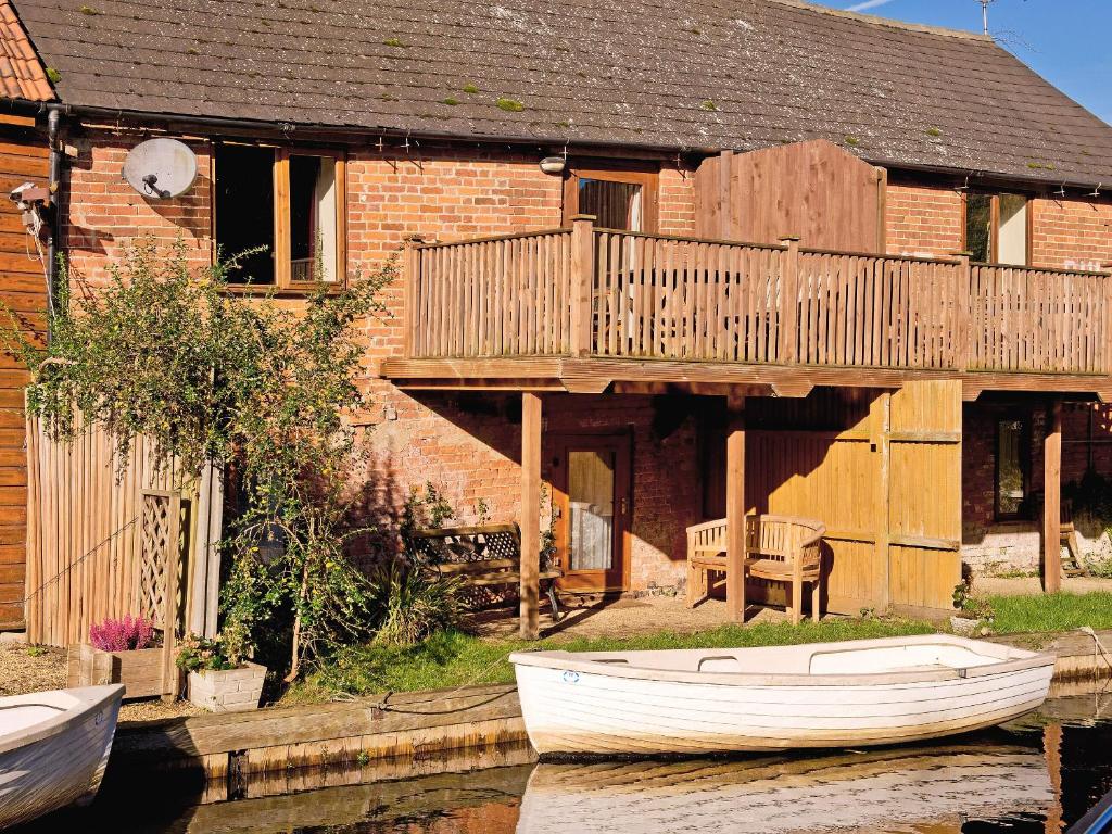 a house with a deck and a boat on the water at Malt Shovel in Dilham
