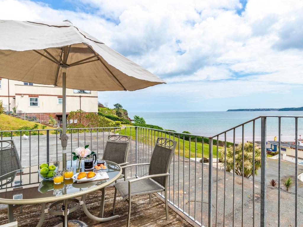 a table with an umbrella on a balcony with the ocean at 7 Vista Apartments in Paignton