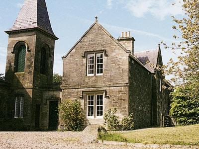 an old stone building with a tower and a church at Lochside Stable Hse in Town Yetholm