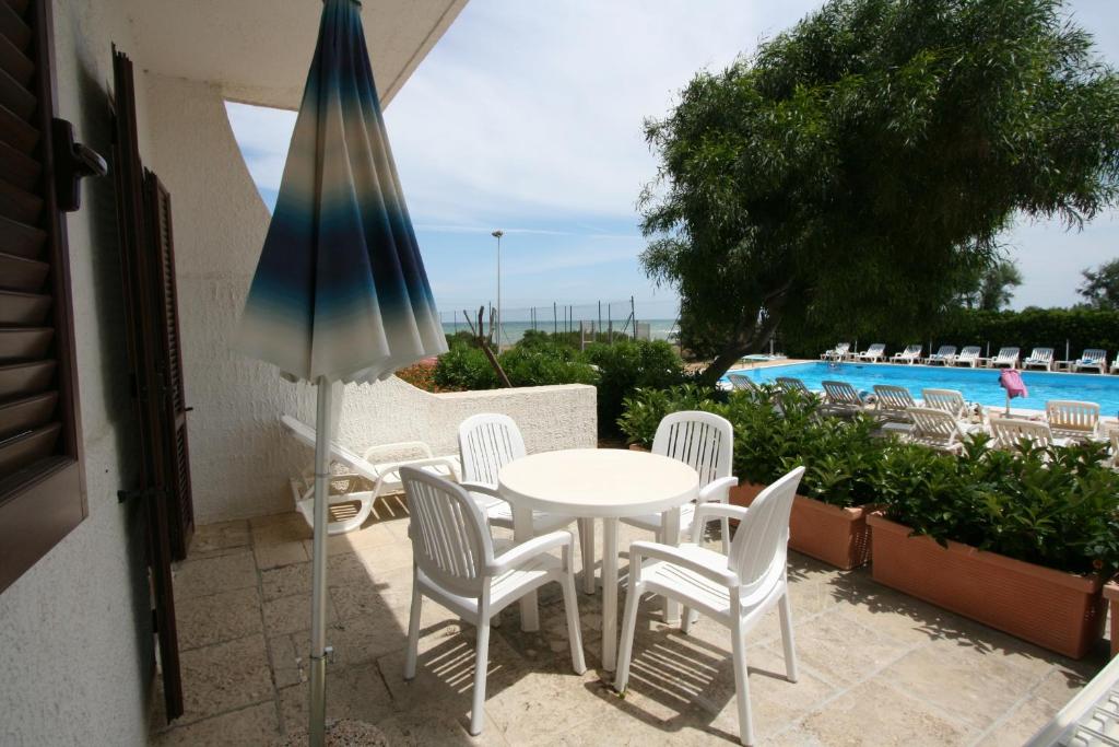 una mesa con sillas y una sombrilla junto a la piscina en Residence Club Barbara, en Ostuni