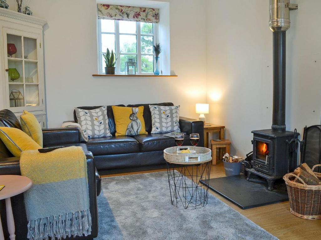 a living room with a black leather couch and a wood stove at Meadowside Forge in Ashwater
