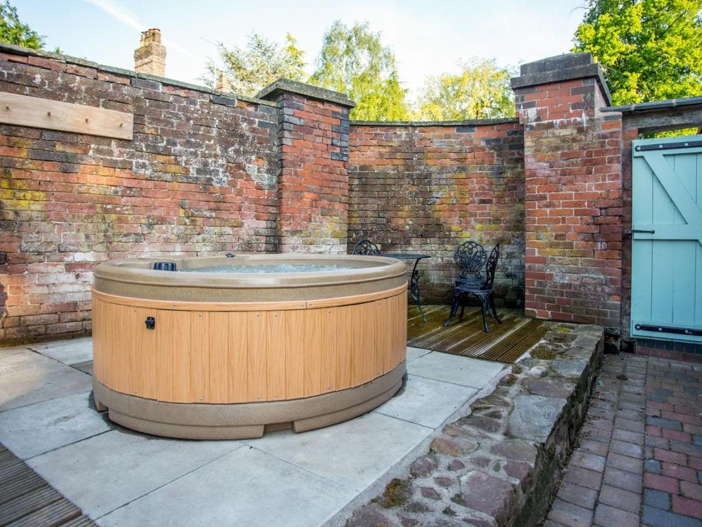 a hot tub on a patio with a brick wall at Betley Court Farm 2 in Betley