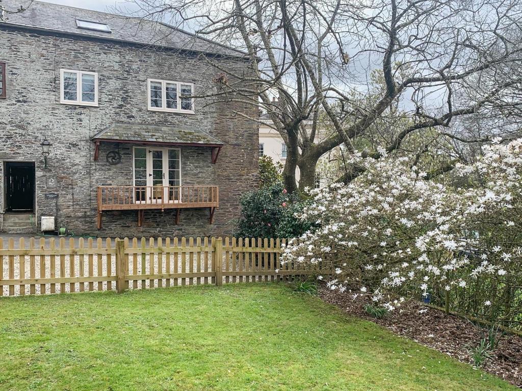 a brick house with a wooden fence and flowers at Hollywell Barn in Menheniot