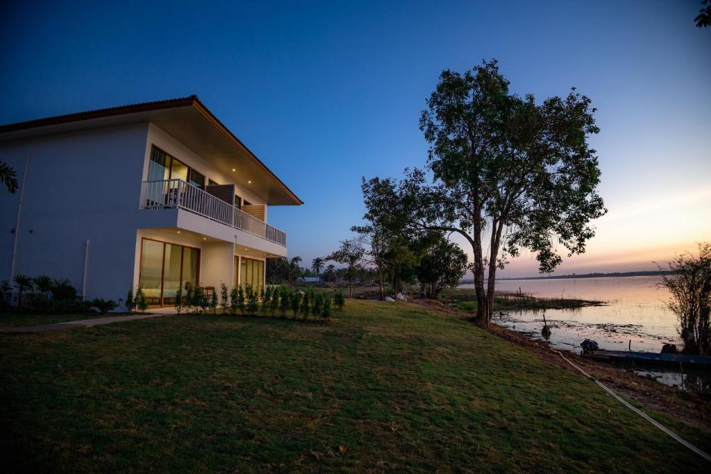 ein Haus mit einem Baum neben dem Wasser in der Unterkunft LAKE HOUSE Naka Cave in Ban Don Klang