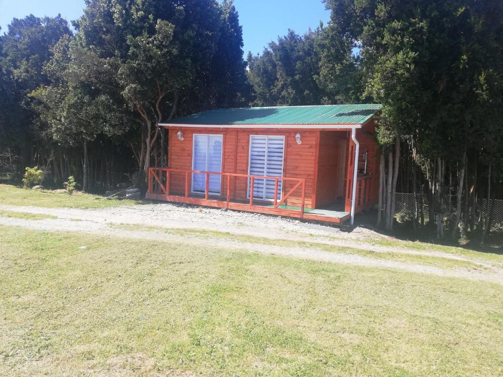 a small red cabin with a green roof on a field at Cabaña entre árboles Carretera Austral in Puerto Montt
