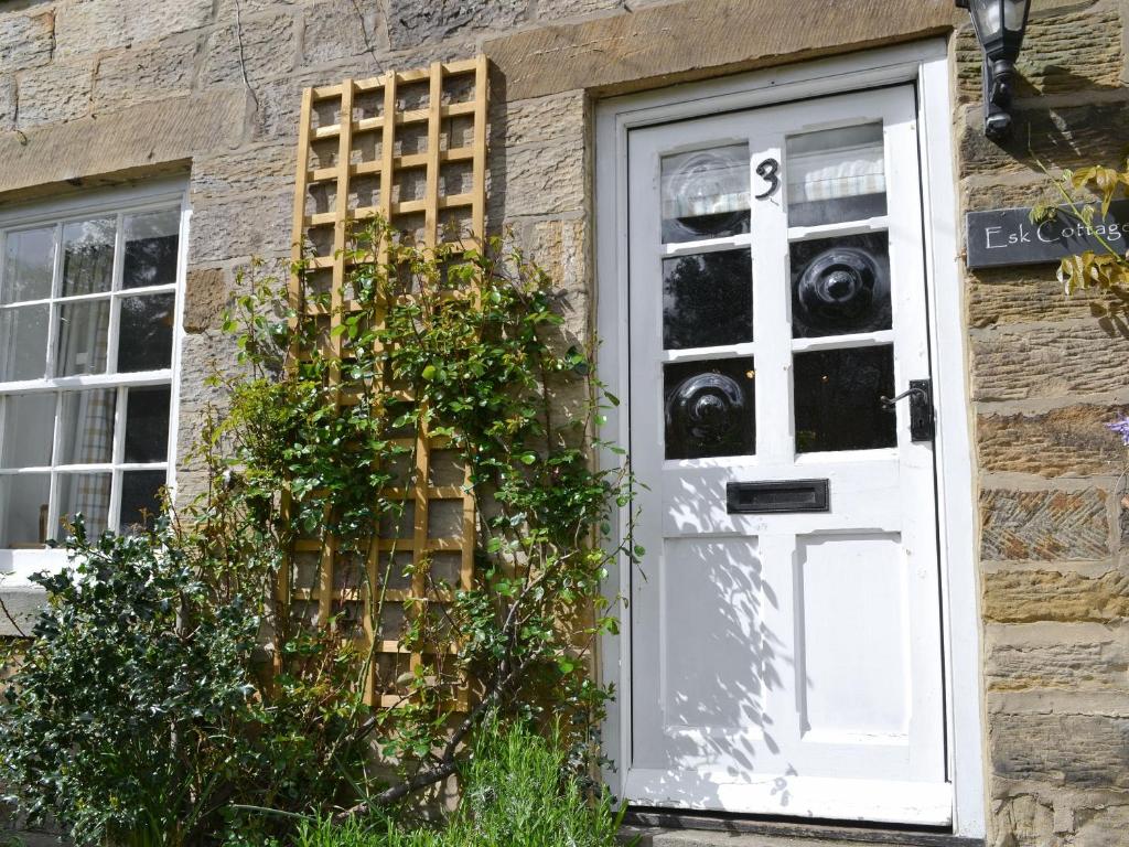a white door on a stone house with plants at Esk Cottage in Egton