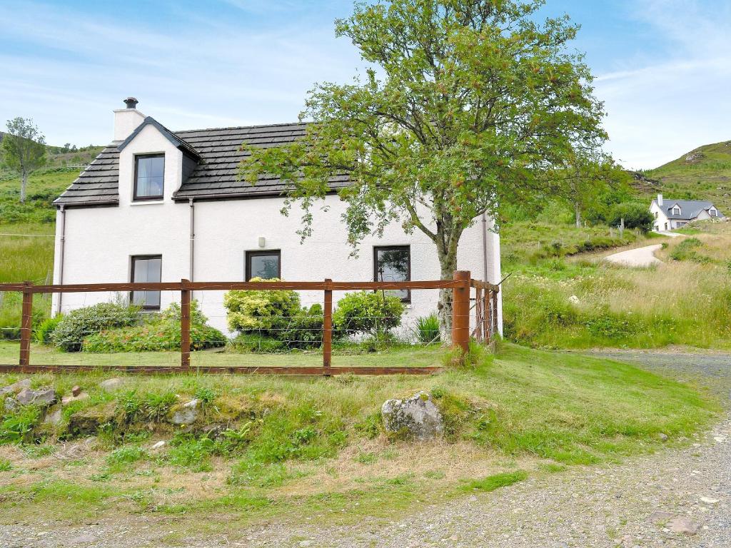 a white house with a wooden fence next to a road at Hannahs Cottage in Inverasdale