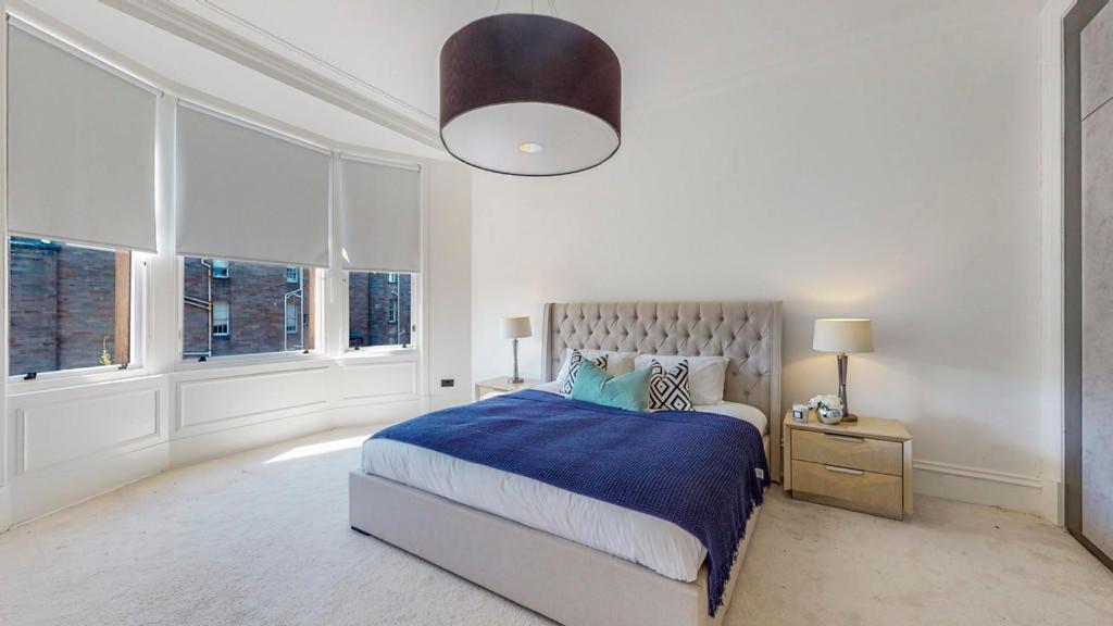 um quarto com uma cama com um cobertor azul e janelas em 69 St Georges Mansions em Glasgow