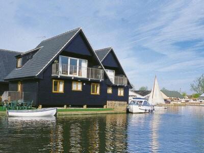 a house on the water with boats in front of it at Heron in Wroxham