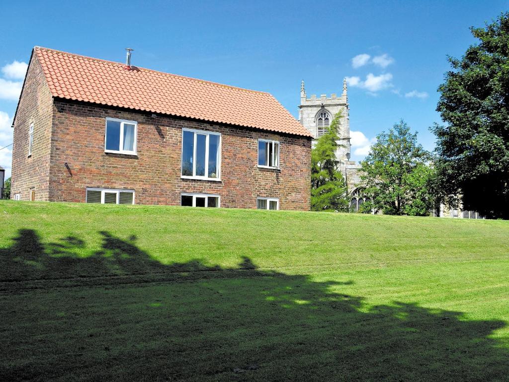 a brick house on a grassy hill with a clock tower at Riverbank Cottage in Althorpe