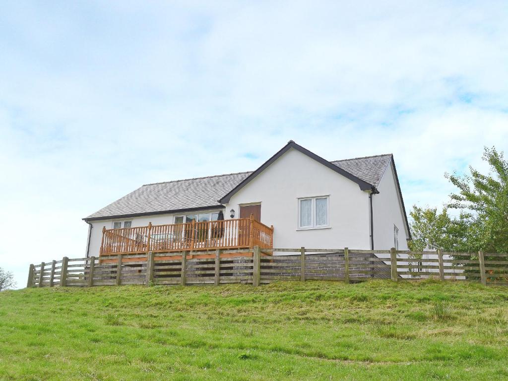 Biały dom na wzgórzu z drewnianym płotem w obiekcie Swallow Cottage w mieście Llanfair Caereinion