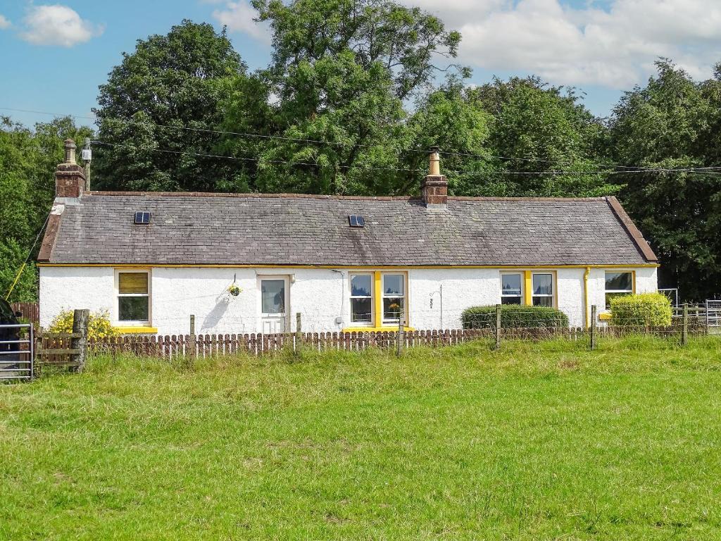 una casa blanca con una valla en un campo en Blaeberry Cottage - 28061, en Dinwoodie Mains