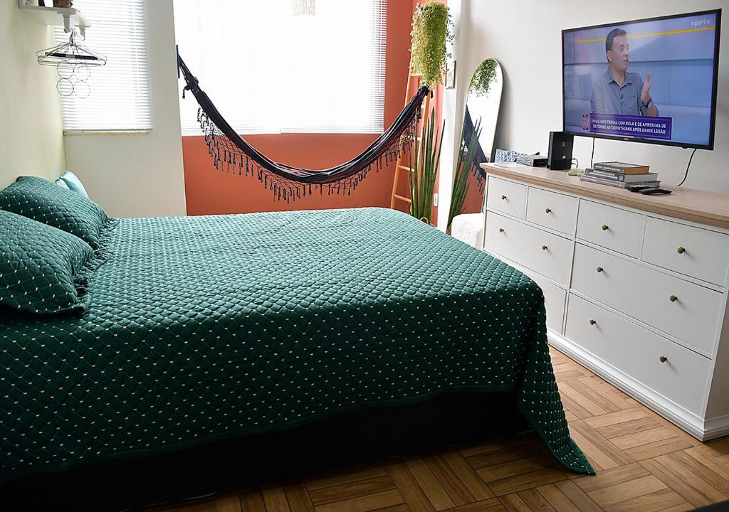 a bedroom with a bed with a green comforter and a tv at Studio Miguel Lemos in Rio de Janeiro