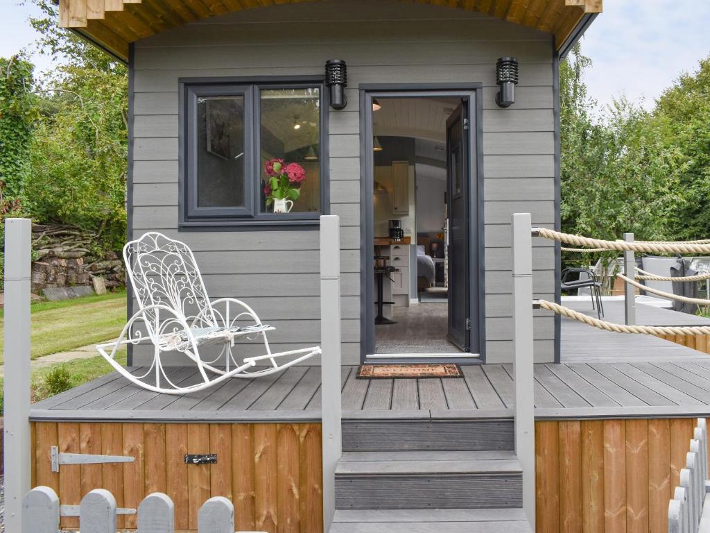 a tiny house with a white chair on a deck at Ponsford Ponds Jacks Shepherd Hut - Bcponhut in Cullompton