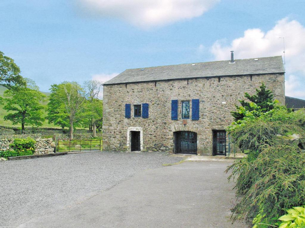an old stone building with blue windows and a driveway at The Barn in Waberthwaite