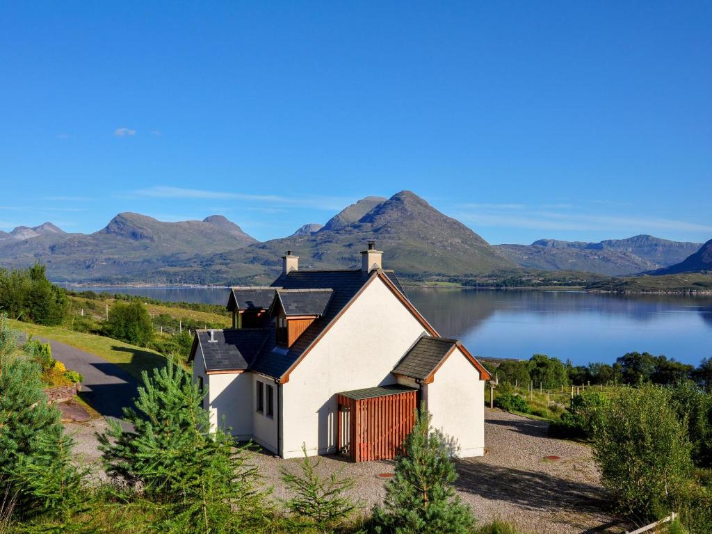 a house on the shore of a lake with mountains in the background at The Narrows in Inveralligin