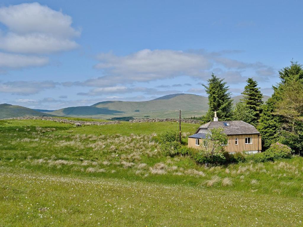 ein altes Haus auf einem Feld mit Bergen im Hintergrund in der Unterkunft Swallow Lodge in Carsphairn