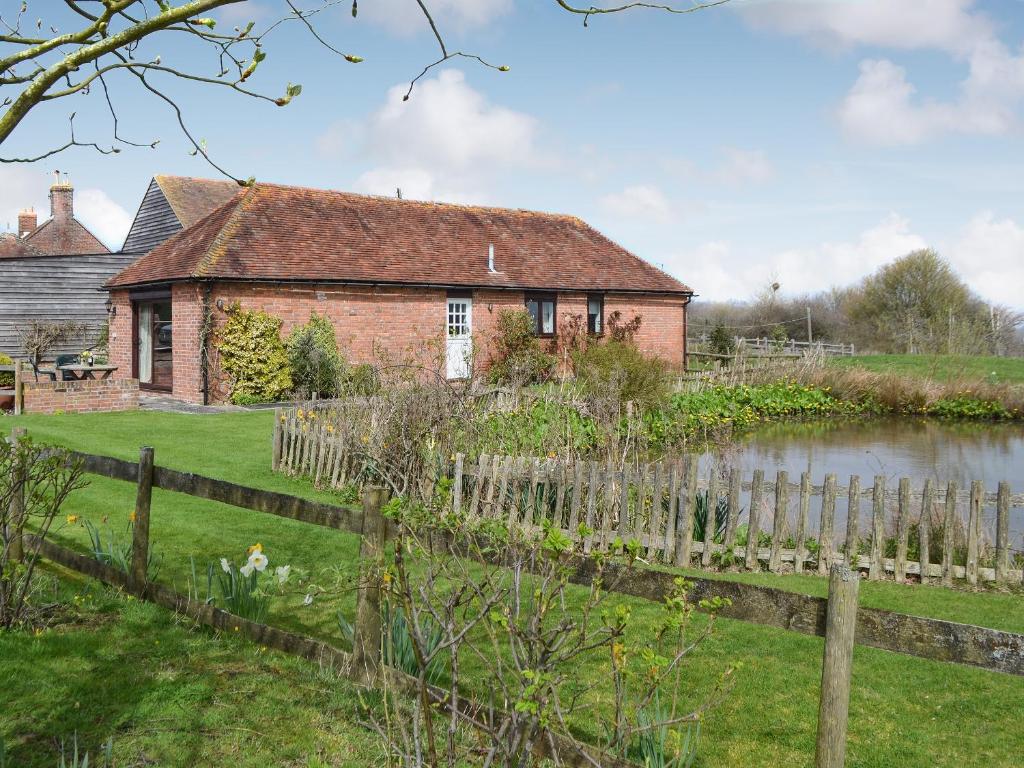 an old brick house with a fence and a pond at Pond Cottage in Peasmarsh