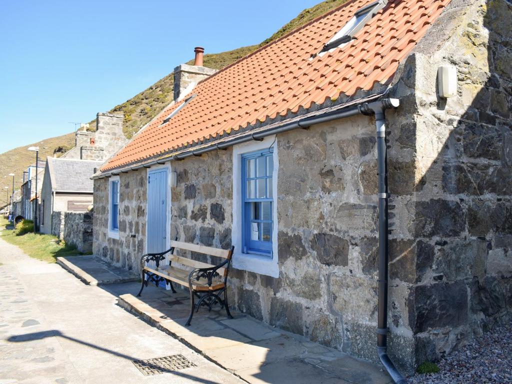 a bench sitting outside of a stone building with blue windows at Crovie in Gardenstown