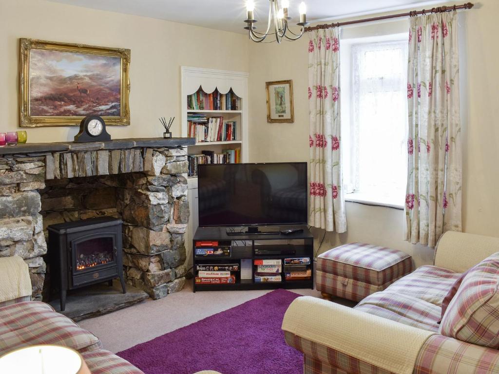a living room with a stone fireplace and a television at Stybarrow View Cottage in Glenridding