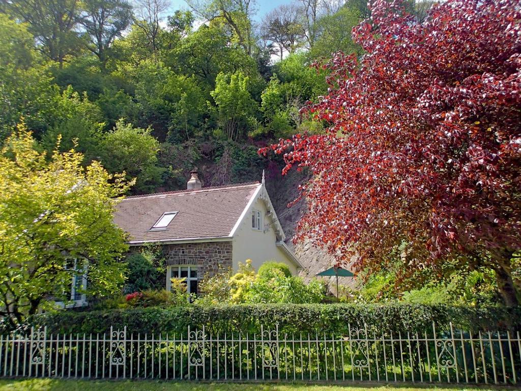 a house behind a fence with a red tree at Heale Cottage - 28087 in Littleham