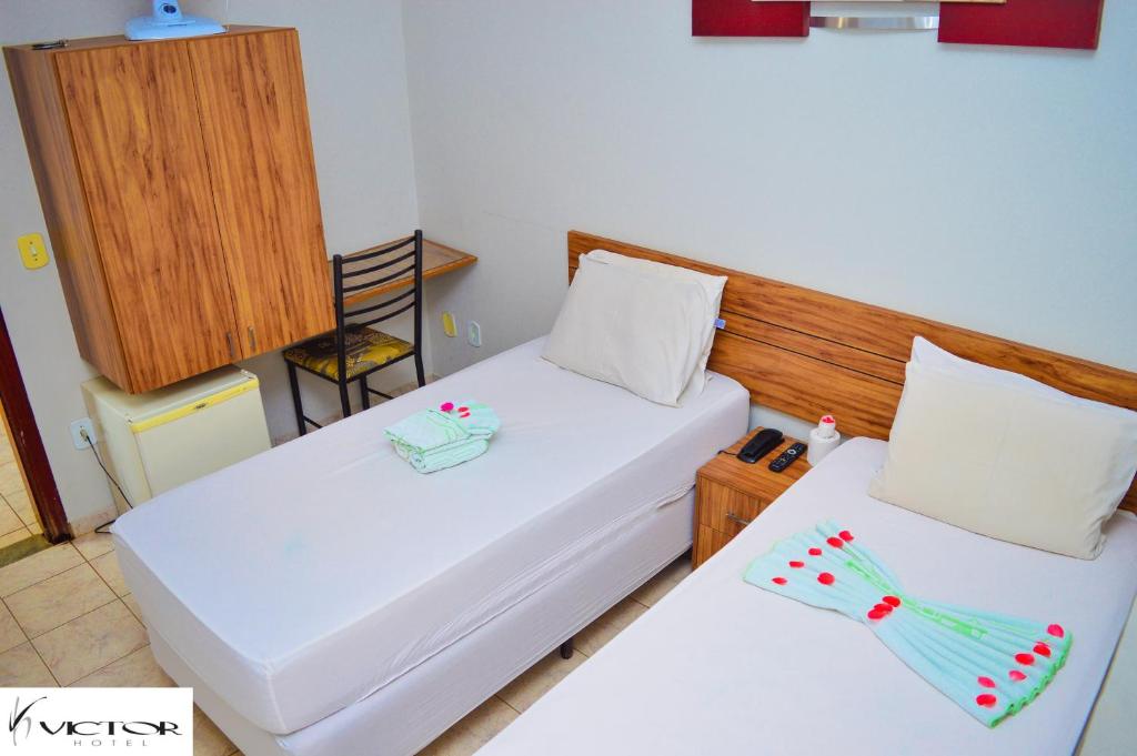 2 bedden in een kleine kamer met witte lakens bij Hotel Victor in Patos de Minas