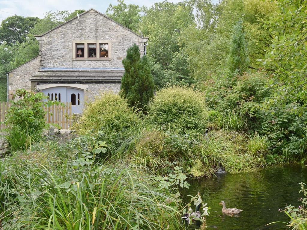 a stone house by a river with two ducks in the water at Sikes Laithe in Kilnsey